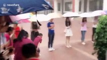 Chinese teachers hold umbrellas for schoolchildren during downpour