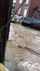 Une femme s’énerve contre une voiture qui passe dans la rue inondée devant chez elle en Belgique