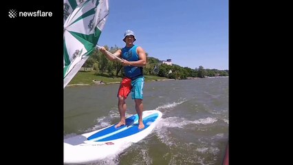 Russian man whizzes across pond using umbrella as sail