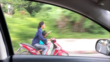 Cette femme en mobylette envoie un texto à deux mains avec son fils assis devant elle