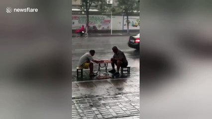 Men play chess calmly in heavy rain