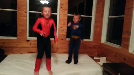Superman and Spiderman jumping on a bed