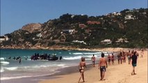 Des migrants en bateau débarquent sur une plage remplie de touristes