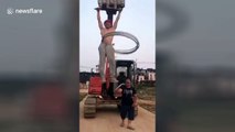 Worker does pull-ups on moving digger while performing hula hoop tricks