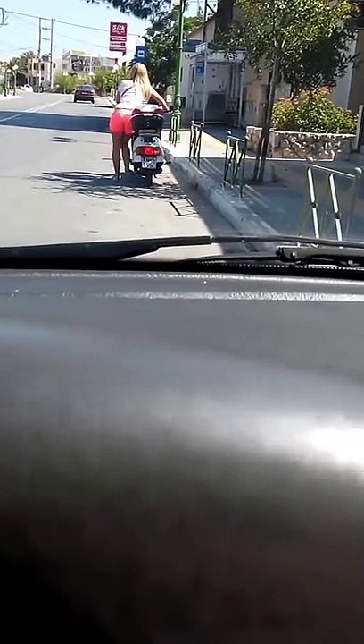 Une fille blonde tente de  démarrer un scooter avec la béquille