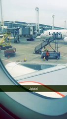 Airport worker flips a cone onto another, dabs, and then dives onto a baggage trolley