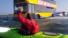 Il fait du kayak sur une route inondée à côté des automobilistes