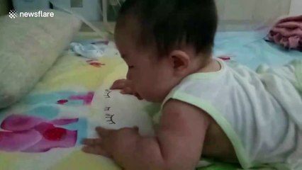 Cute baby tries to eat strawberry pattern on bed sheet