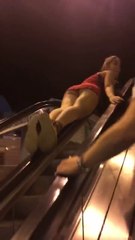 Une femme en robe monte sur la rambarde de l'escalator et chute