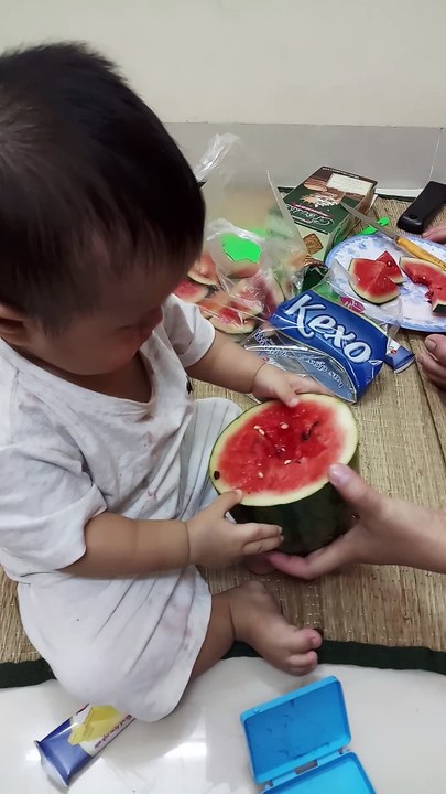 The 8-month-old baby is holding a piece of watermelon on his own