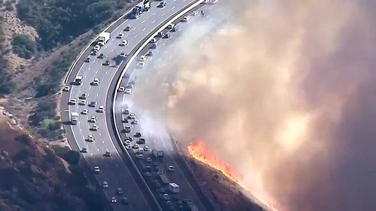 Un hélicoptère largue de l'eau sur une autoroute au bord des flammes (Californie)