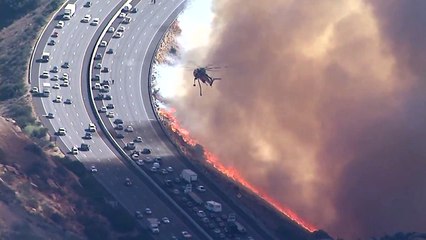 Un hélicoptère largue de l'eau sur une autoroute au bord des flammes (Californie)
