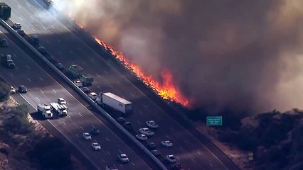 Un hélicoptère largue de l'eau sur une autoroute au bord des flammes (Californie)