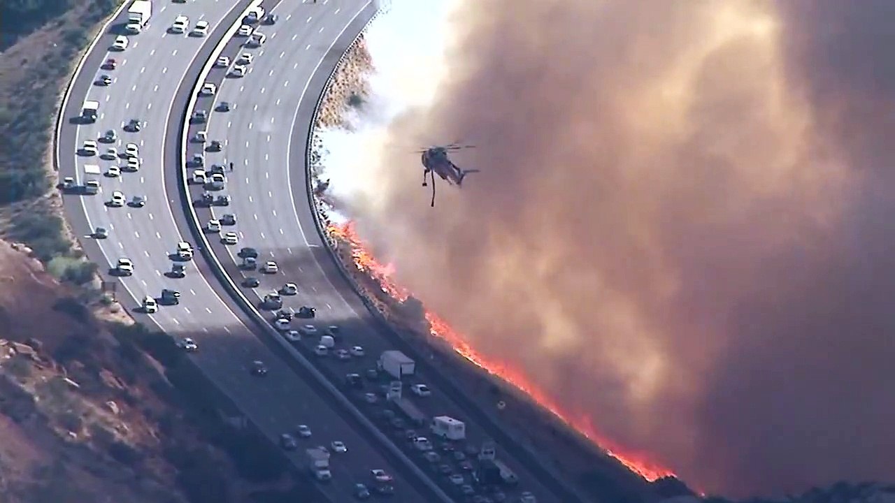 Un hélicoptère largue de l’eau sur une autoroute qui se fait attaquer par les flammes en Californie