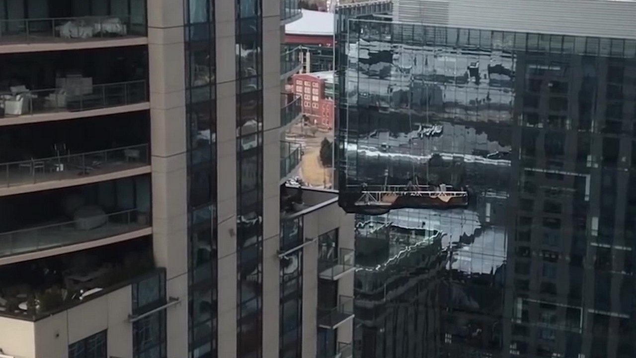 Des laveurs de vitres sur une nacelle se font malmener par le vent et s'encastrent dans une fenêtre