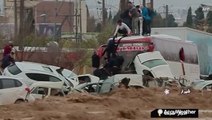 People climb onto vehicles tossed around by powerful floodwaters to escape drowning