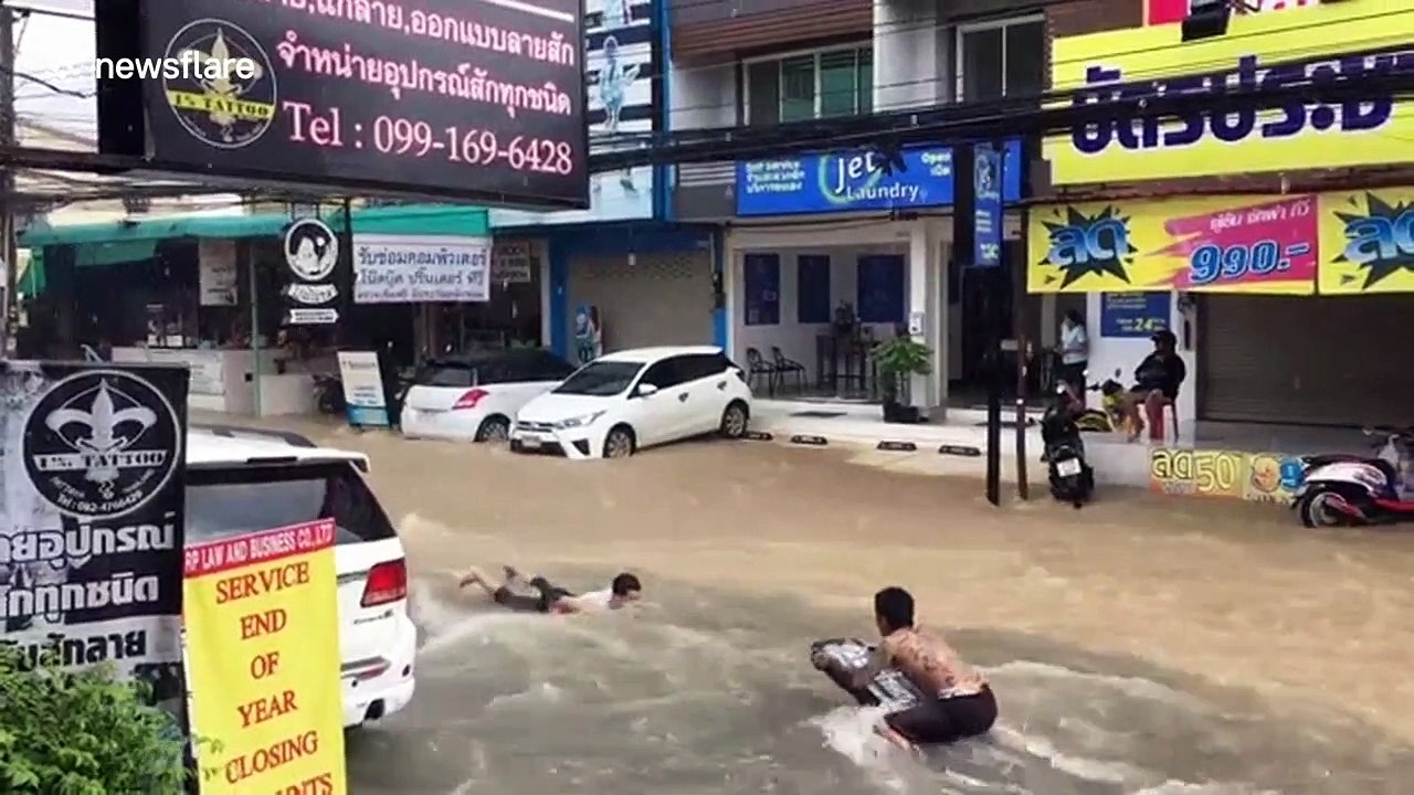 Boys go bodyboarding on flooded road in Thailand