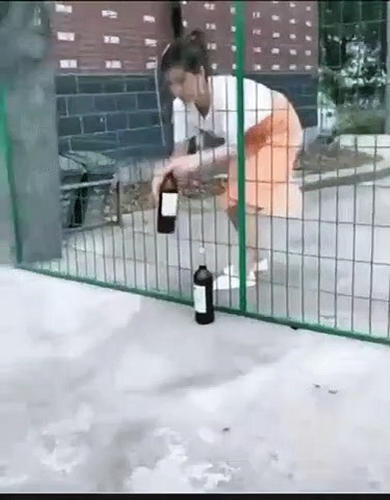 Un jeune garçon trolle une femme qui fait passer une bouteille de vin à travers un grillage