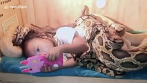 Indonesian girl calmly watches cartoons on phone while covered head to toe in snakes