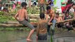 Contestants whack each other with bags of rice while balancing on pole over pool of mud in Indonesia