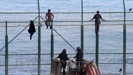 Algunos inmigrantes esperan bajar de la valla tras un asalto masivo en Ceuta.