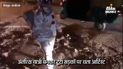 अंतरिक्ष यात्री जैसे कॉस्ट्यूम में गड्ढों वाली सड़क पर मूनवॉक की तरह चला कलाकार