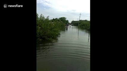 Indian man carries motorbike on shoulder over flooded road so it doesn't get wet
