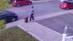 Une femme qui marche dans la rue balance violemment une poubelle sur une voiture