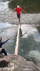 Un homme traverse une rivière suri un tronc d'arbre