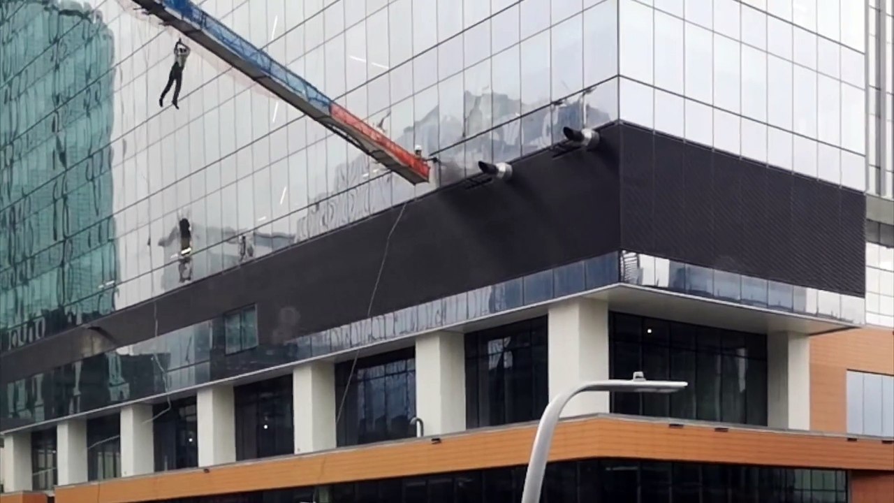 La nacelle de laveurs de vitres se balance au vent contre le gratte ciel !