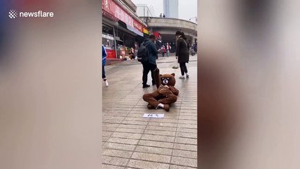 Chinese man in bear costume lays on floor while handing out leaflets