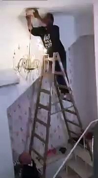Un homme essaye d’accrocher un lustre en haut des escaliers