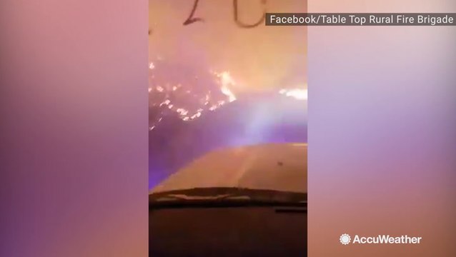 Firefighters drive down road surrounded by wildfire