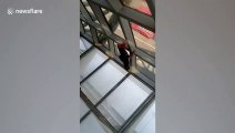 Thai airport security guard inches along glass ceiling to retrieve tourist's dropped phone