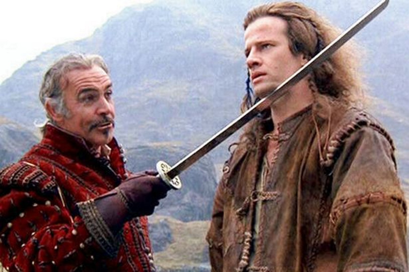 An image from the film Highlander. Sean Connery holds a sword under the chin of French actor Christophe Lambert. His hair is long, slightly wild, with plaits at the side. 