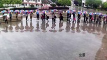 Chinese teachers hold umbrellas in a line for pupils during downpour
