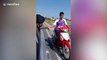 Thai policeman in car holds motorcyclist's hand to drag him home after his motorbike runs out of fuel