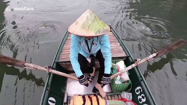 Woman squeezes boat through narrow gaps in the rock as tourists explore caves in Vietnam