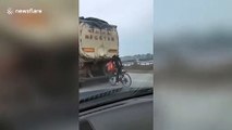 Chinese cyclist holds onto back of truck to be dragged along road