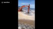 Smart excavator driver uses crane to rescue another vehicle being submerged by ocean waves
