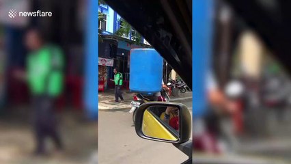 Motorcycle passenger in Indonesia rides with huge blue water tank over his body