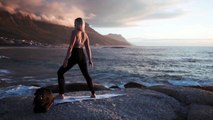 Woman Meditating In Yoga Warrior Pose At The Ocean, Beach  And Rock Mountains.