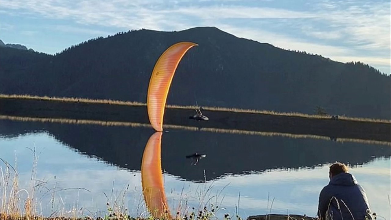 Paraglider is perfectly reflected in lake as he spirals above the water
