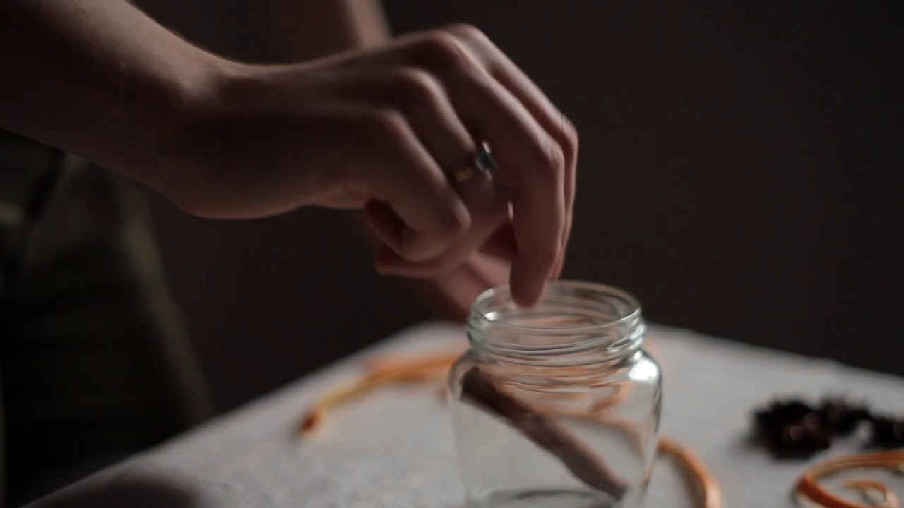 _Young_Woman_Adds_Cinnamon_Orange_Peel_Spices_to_Jar_Cooking