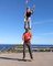 Guy Stands On Balance Board While Woman Stands On His Shoulders And Juggles