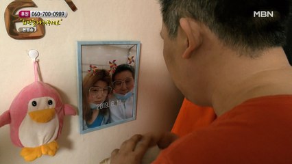 아내와 같이 찍은 사진을 벽에 걸어둔 남편