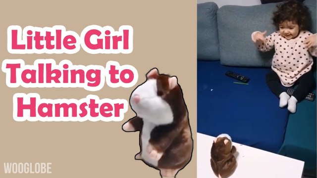 'Adorable baby girl having an interesting conversation with talking hamster toy'