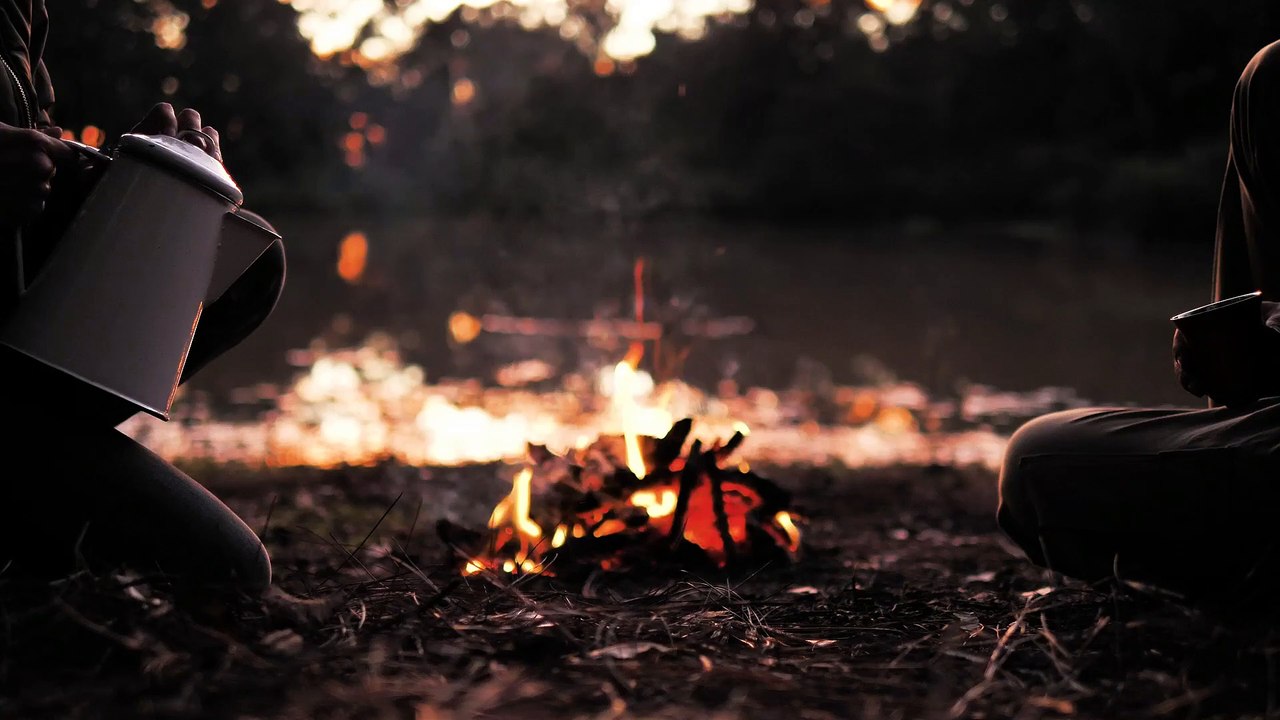 People sharing a warm drink around a camp fire in the early evening.