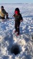 Ce garçon pêche un poisson aussi grand que lui sur un lac gelé