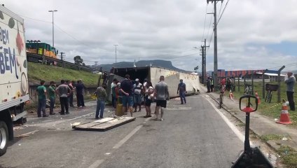 Pessoas retiram parte da carga de aves congeladas em caminhão que tombou na BR